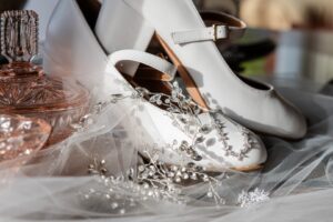 Close-up of bridal shoes with crystal embellishments on a veil, alongside a vintage glass perfume bottle.