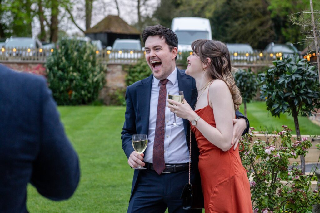 A man and a woman laughing and enjoying a conversation with drinks in their hands at a garden party setting.