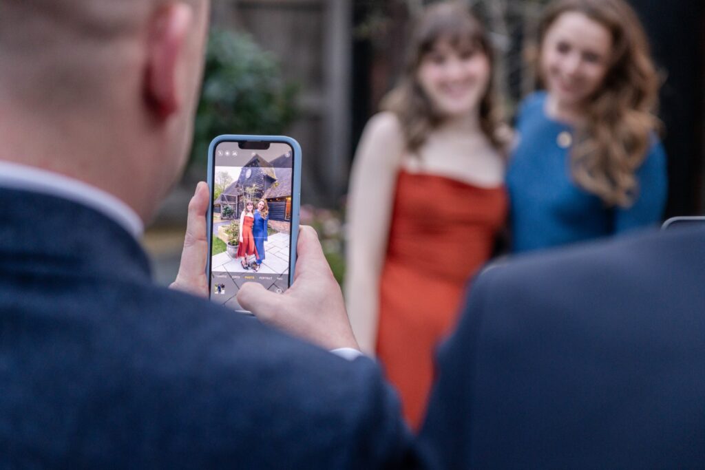 A person takes a photo of two smiling women on a smartphone, with the focus on the phone screen.