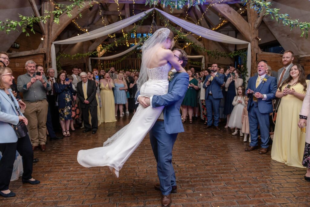 A smiling bride and groom sharing their first dance while guests look on in a festively decorated hall.