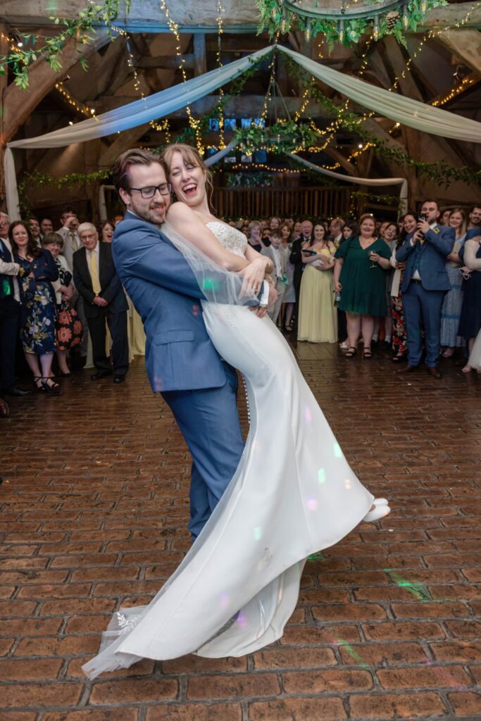 A bride and groom dancing happily during their wedding reception, surrounded by smiling guests.