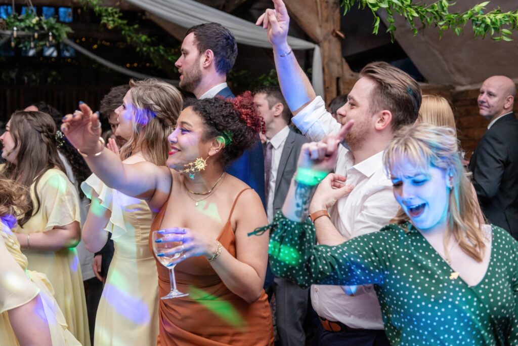 Group of people dancing and having fun at an indoor celebration with colorful lights casting patterns on them.