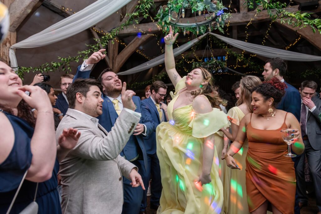 A group of people dancing and having a great time at a wedding reception, with colorful lights illuminating their joyous expressions.