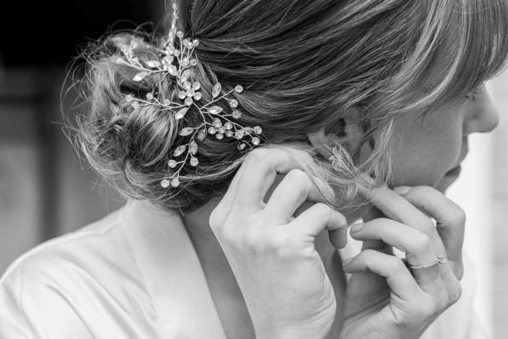 A close-up grayscale photo of a bride fixing her earring with an elegant hairstyle and a decorative hairpiece visible.