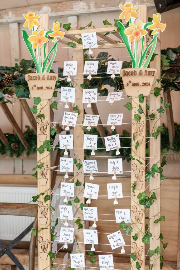 A wooden wedding seating chart with names and strings, decorated with illustrations of flowers and the names Jacob & Amy with a wedding date displayed at the top.