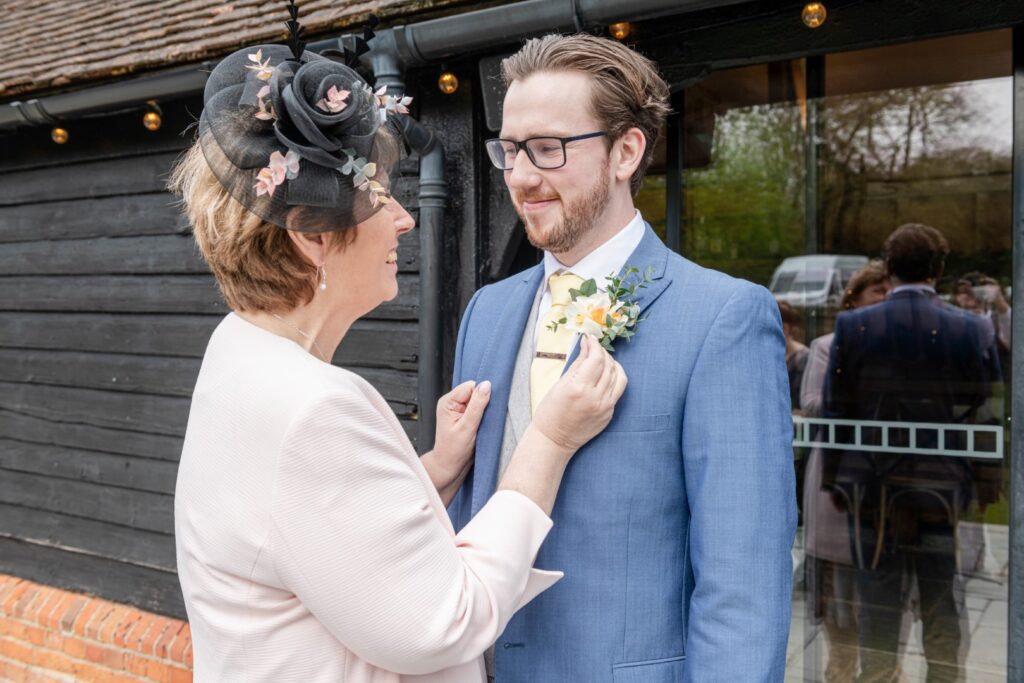 A smiling woman adjusts a boutonniere on a man's suit lapel before a formal event.