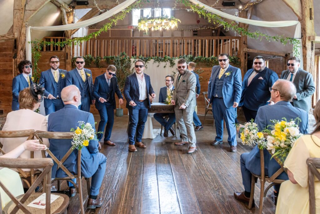 Group of groomsmen walking down the aisle at a barn wedding ceremony with guests seated on either side.