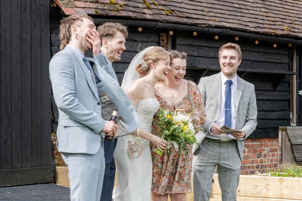 A group of people laughing and enjoying a happy moment at a wedding ceremony, with a bride holding a bouquet.