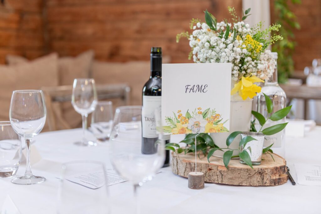 A sophisticated dinner table setup with empty glasses, a wine bottle, floral decorations, and an event table number card with the word 'FAME'.