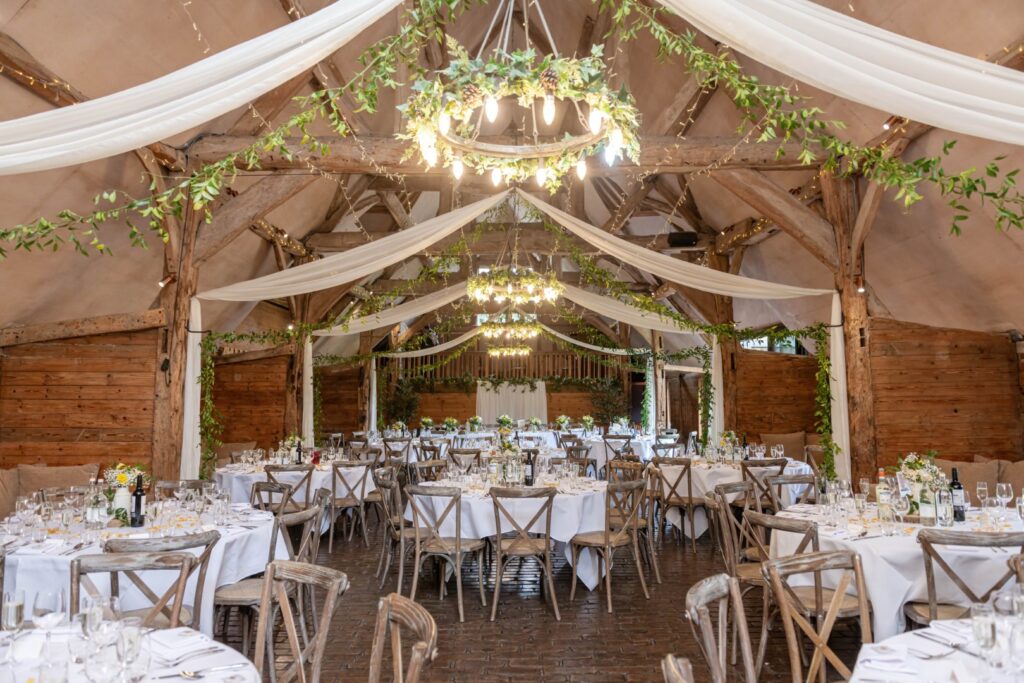 Interior view of a rustic wedding venue with wooden beams, draped fabric, and table settings ready for guests.