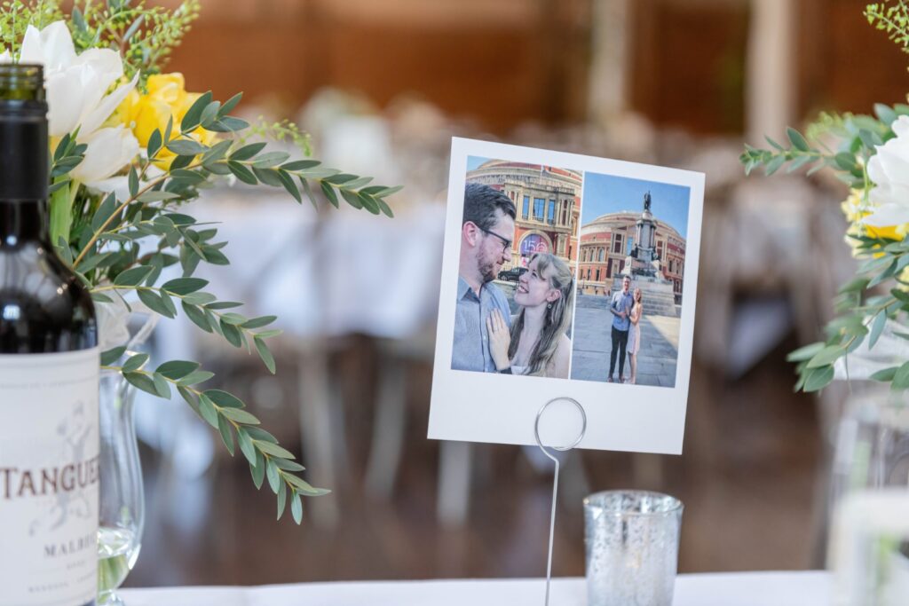 A table setting at a wedding with a bottle of wine, floral decorations, and a photo holder displaying a picture of a couple.