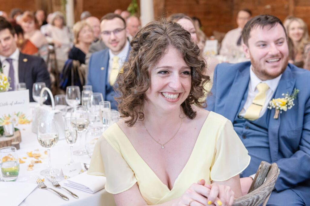 A smiling woman in a yellow dress at a wedding reception, with guests in the background.