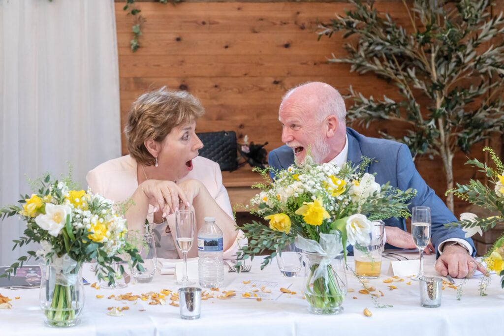 Two people joyfully engaging in conversation at a decorated table with flowers and drinks during a celebration.