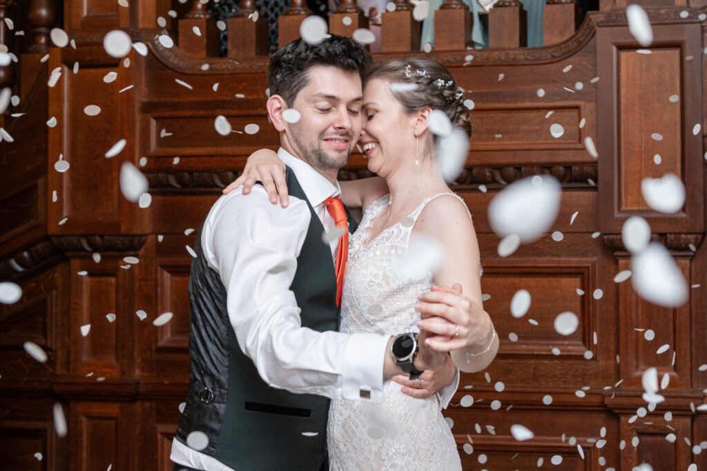 Couple dancing joyfully at their wedding, surrounded by falling petals in a beautifully decorated venue.