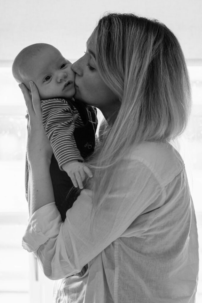 A mother kisses her baby while holding him close, capturing a heartfelt moment in black and white.