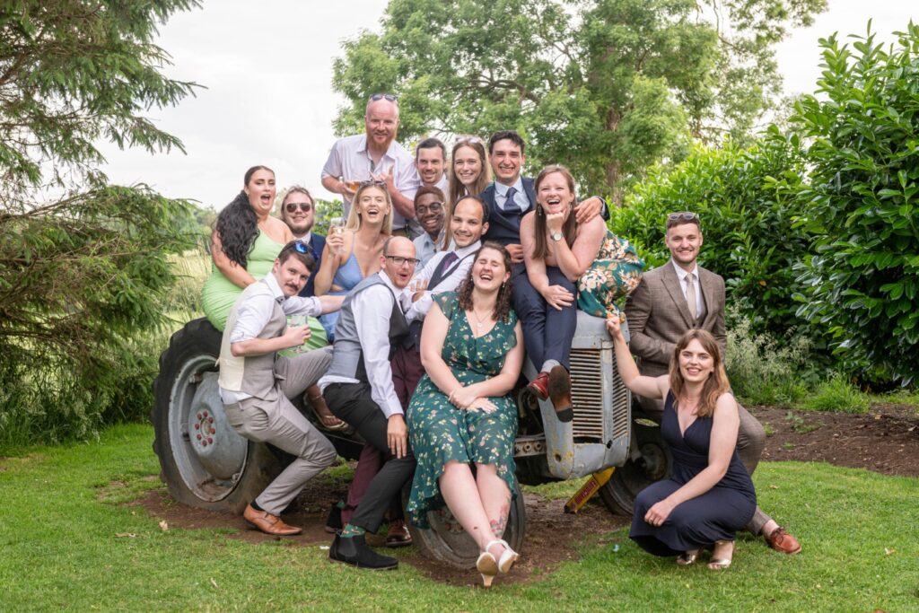 A lively group of friends joyfully posing on a vintage tractor in a lush outdoor setting at Ashton Lodge